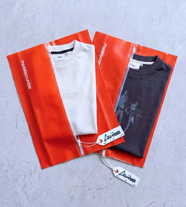 Two t-shirts, one white and one gray, in red PVC packaging with a brand tag on a gray surface.