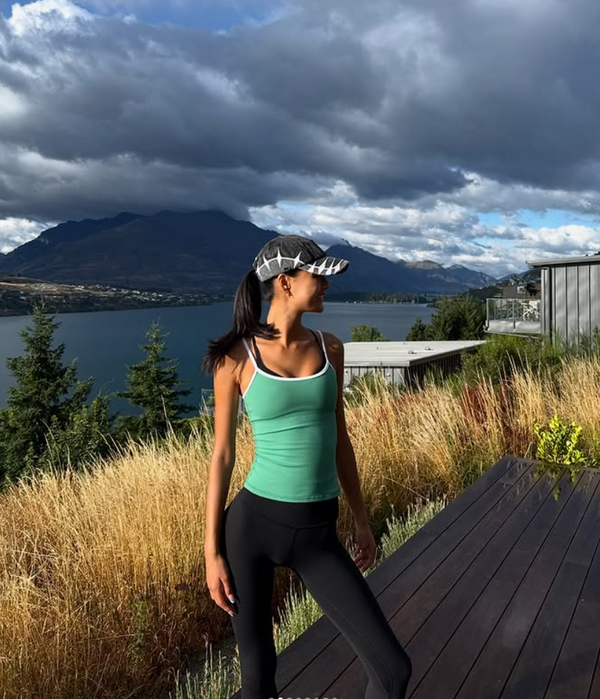 Person in athletic wear wearing a distressed two tone cap, standing on a wooden deck with mountains and lake in the background