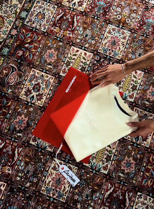 Person opening a red PVC bag on a persian carpet pulling out a heavy weight boxed fitted t-shirt.