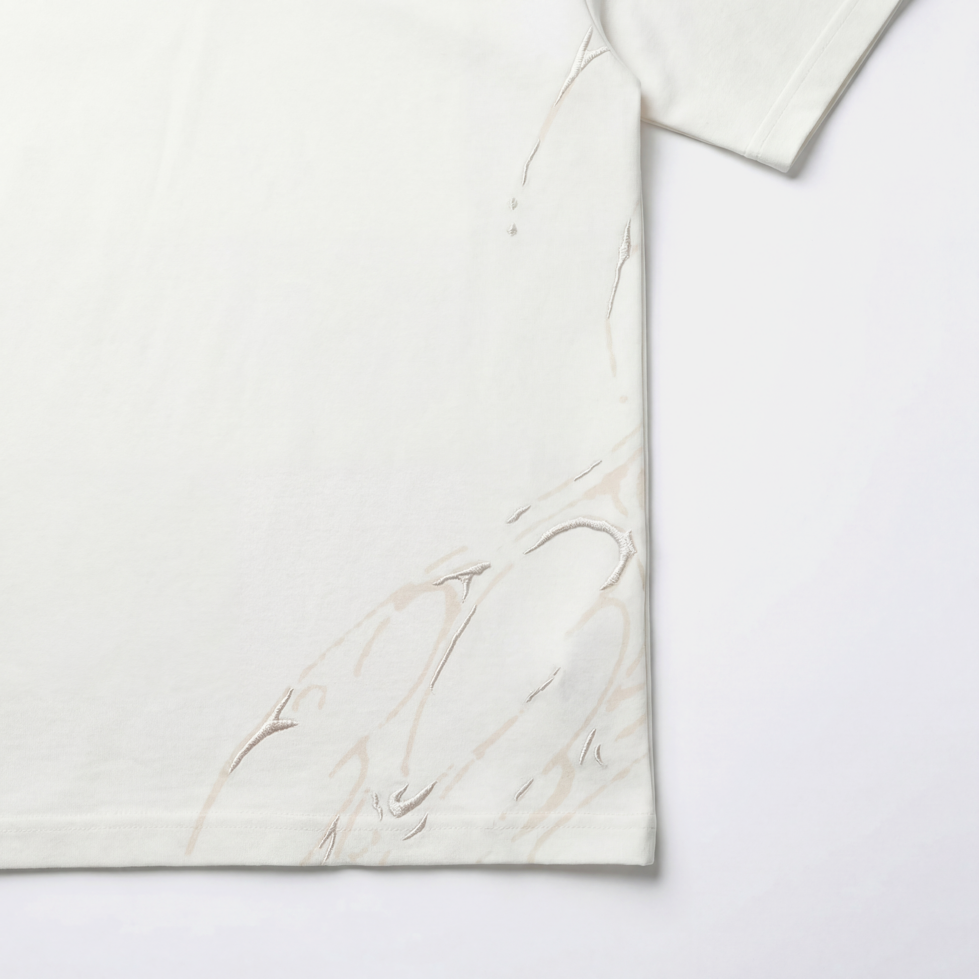 White AVALIN tee, lower side screen print with embroidered detailing visible from back.